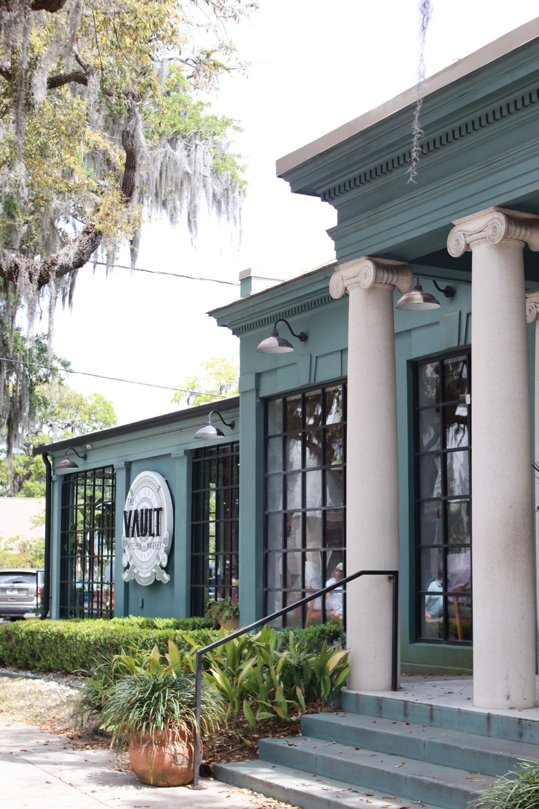 Teal storefront with white columns, glass doors, and potted plants by the entrance