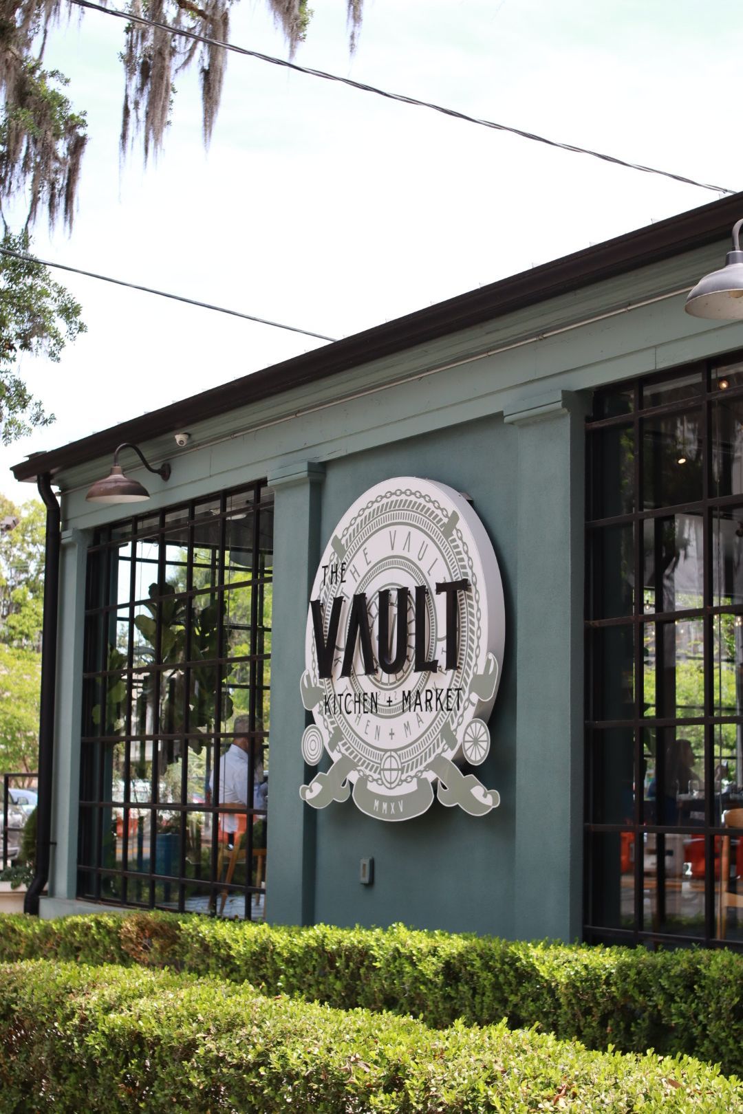 Exterior of The Vault storefront with green walls, barred windows, and hedge landscaping