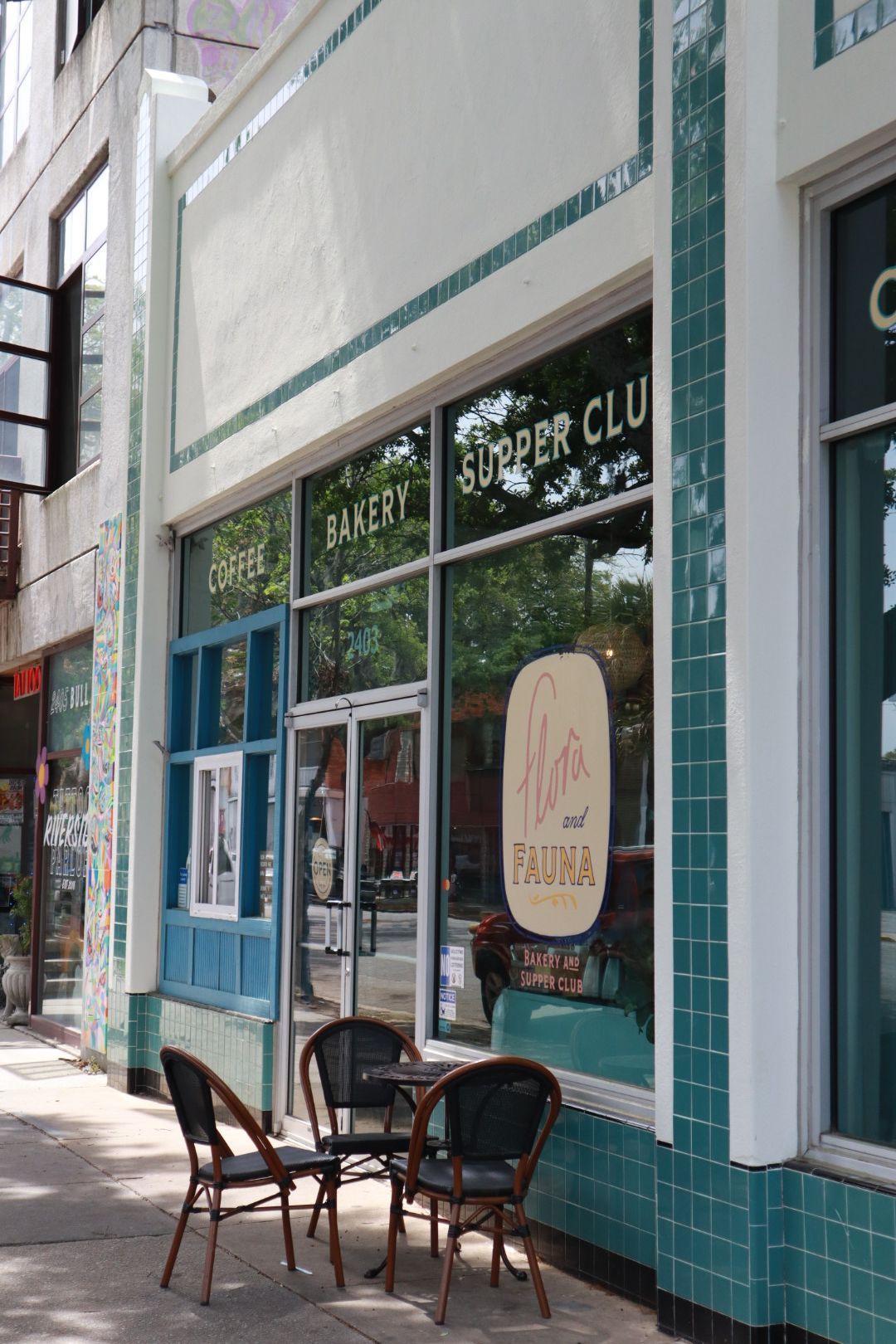 Storefront with teal tile facade, large windows, and two chairs on the sidewalk