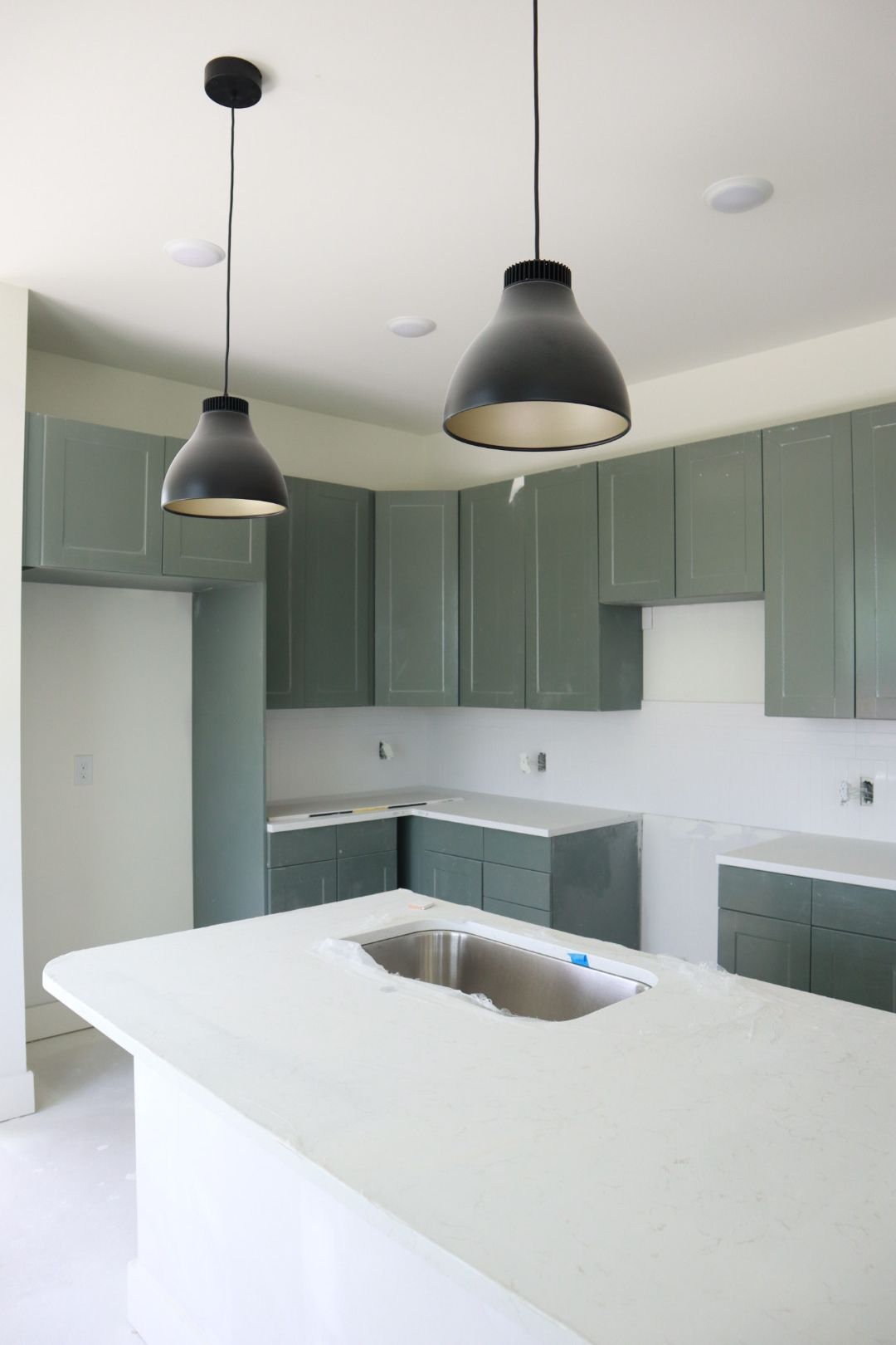 Modern kitchen with sage green cabinets, white island, and black pendant lights