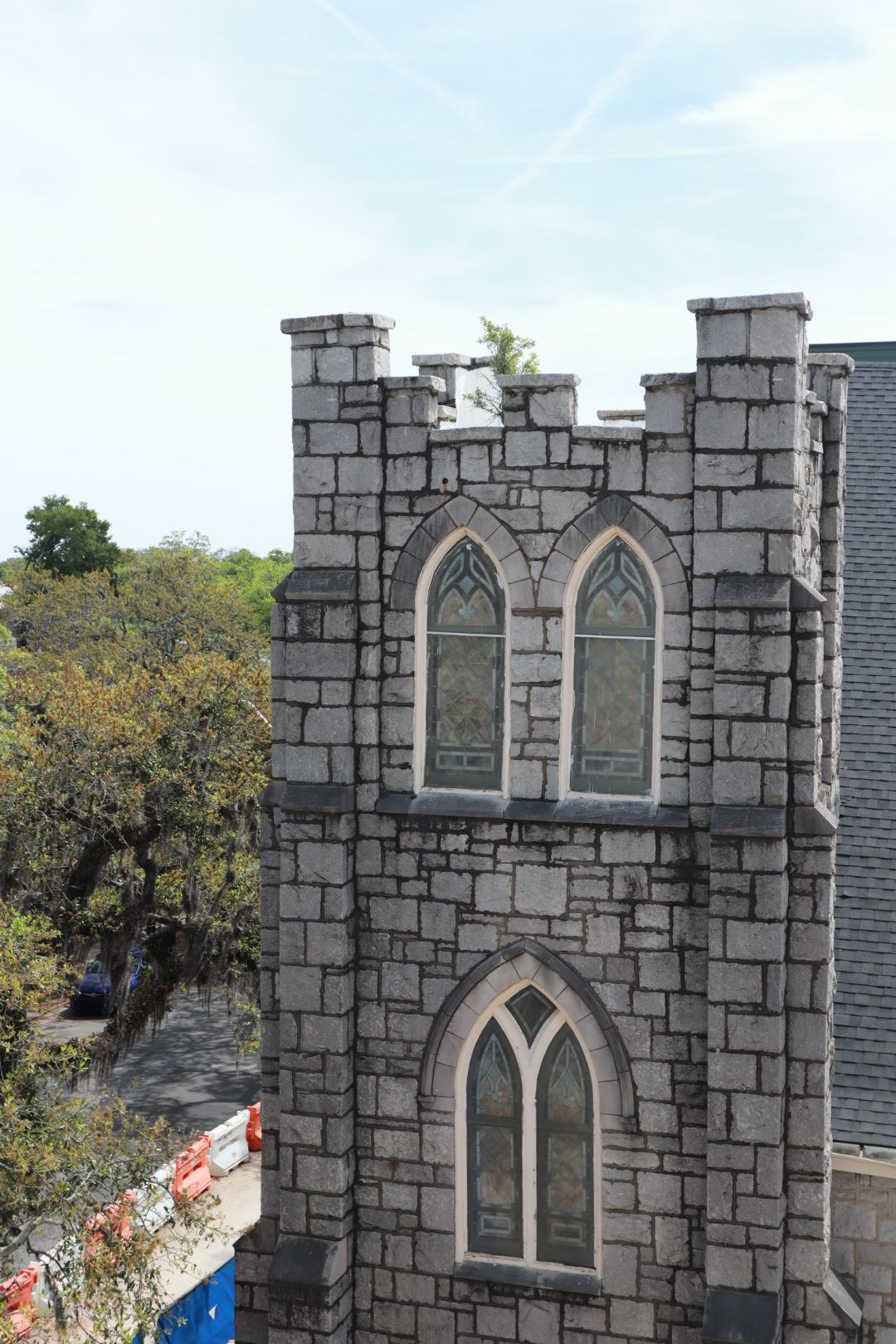 Stone tower with pointed arched windows beside trees under a pale sky