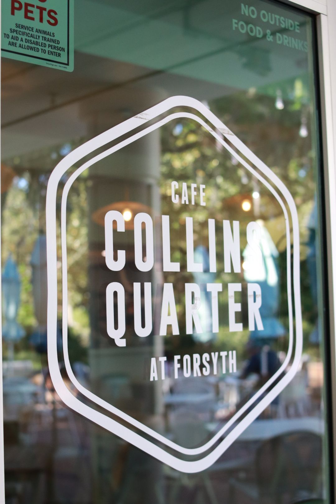 Cafe Collins Quarter logo on a glass door, with white lettering inside a hexagon outline.