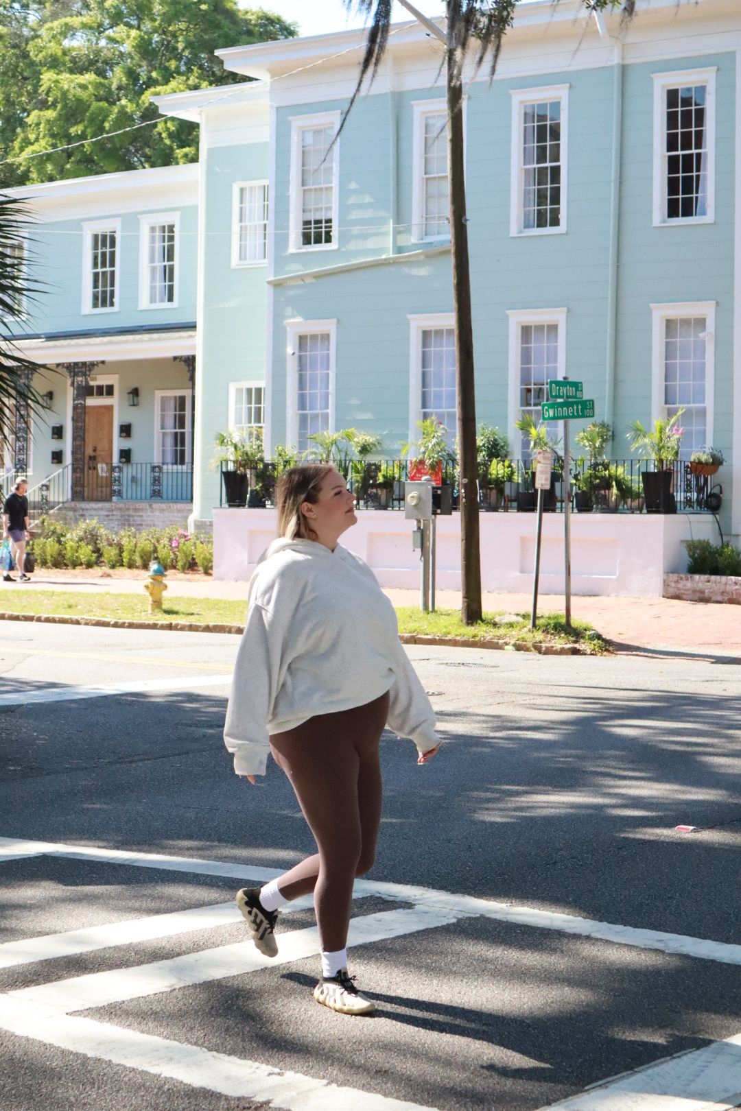 Person crossing a street in front of a pastel blue building on a sunny day