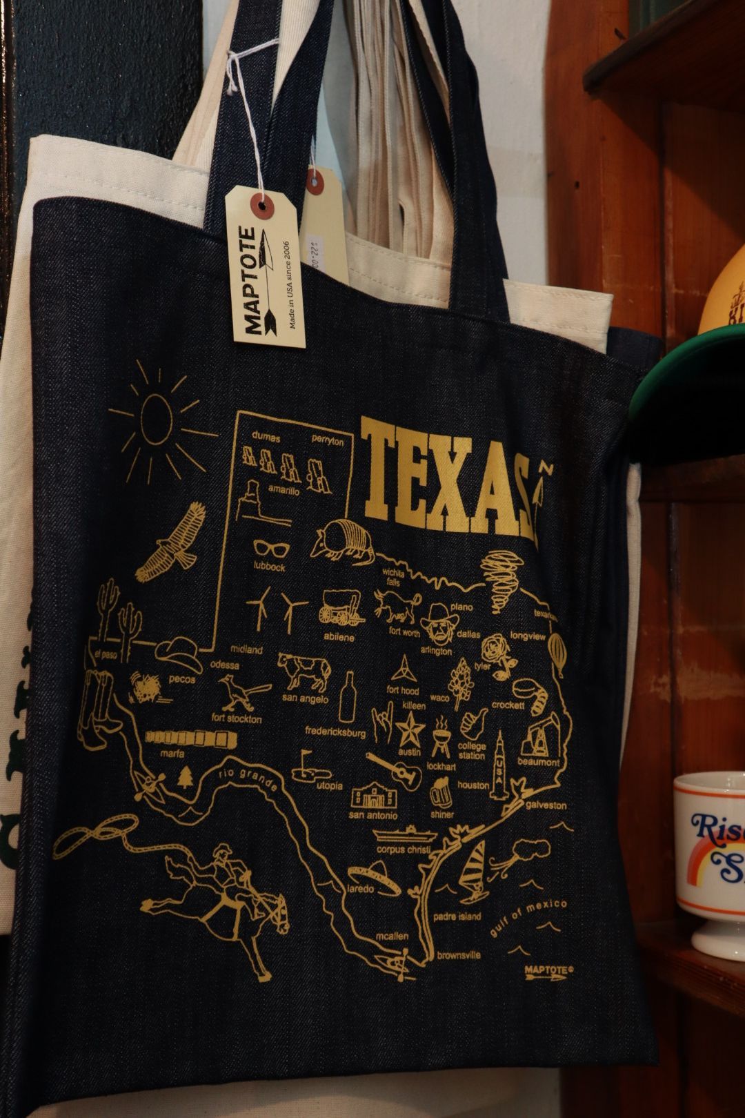 Black tote bag with gold Texas map design and white handles hanging indoors.