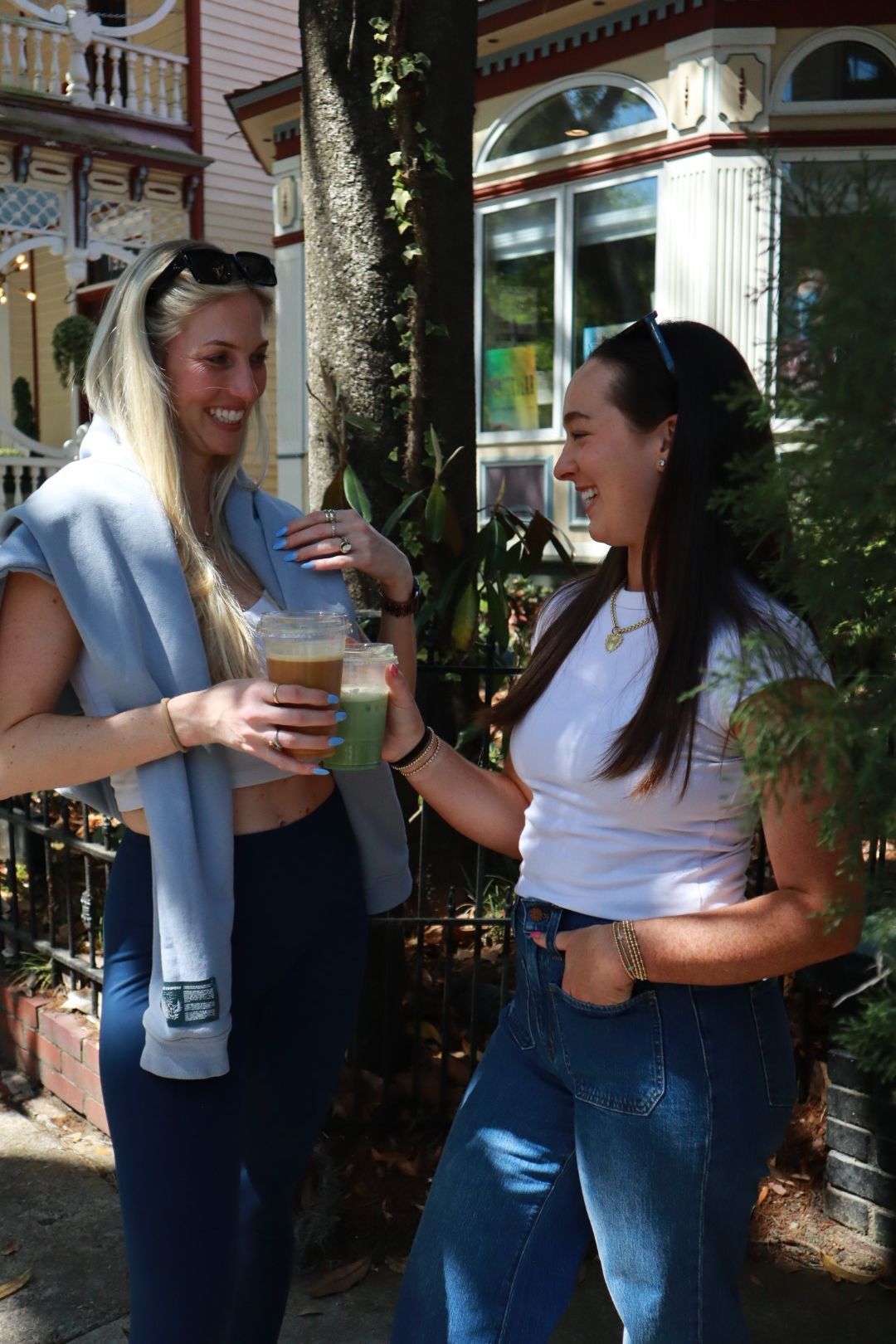 Two women chatting outdoors, one holding a clear drink cup by a storefront.