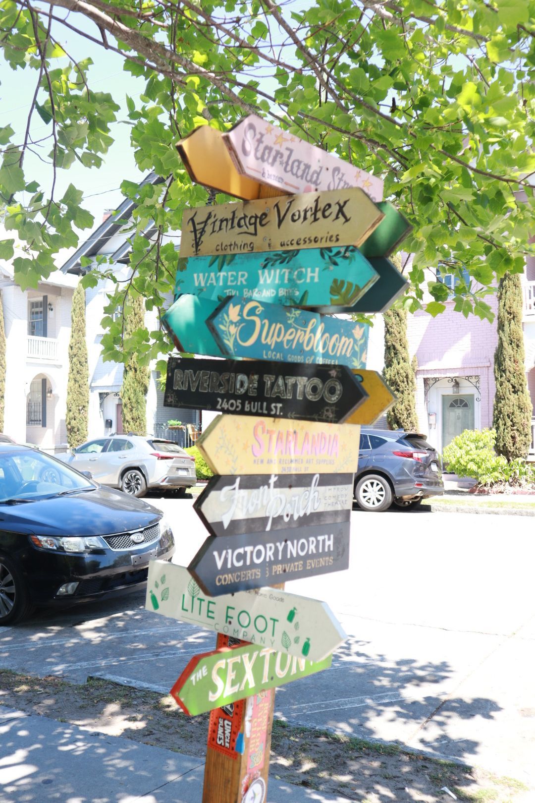 Colorful directional signpost with arrows to local attractions on a sunny street with parked cars and trees