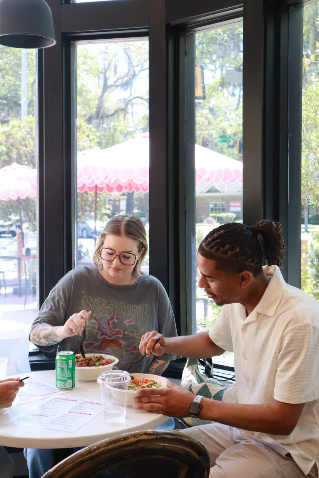 Two people eating together at a cafe table by large windows