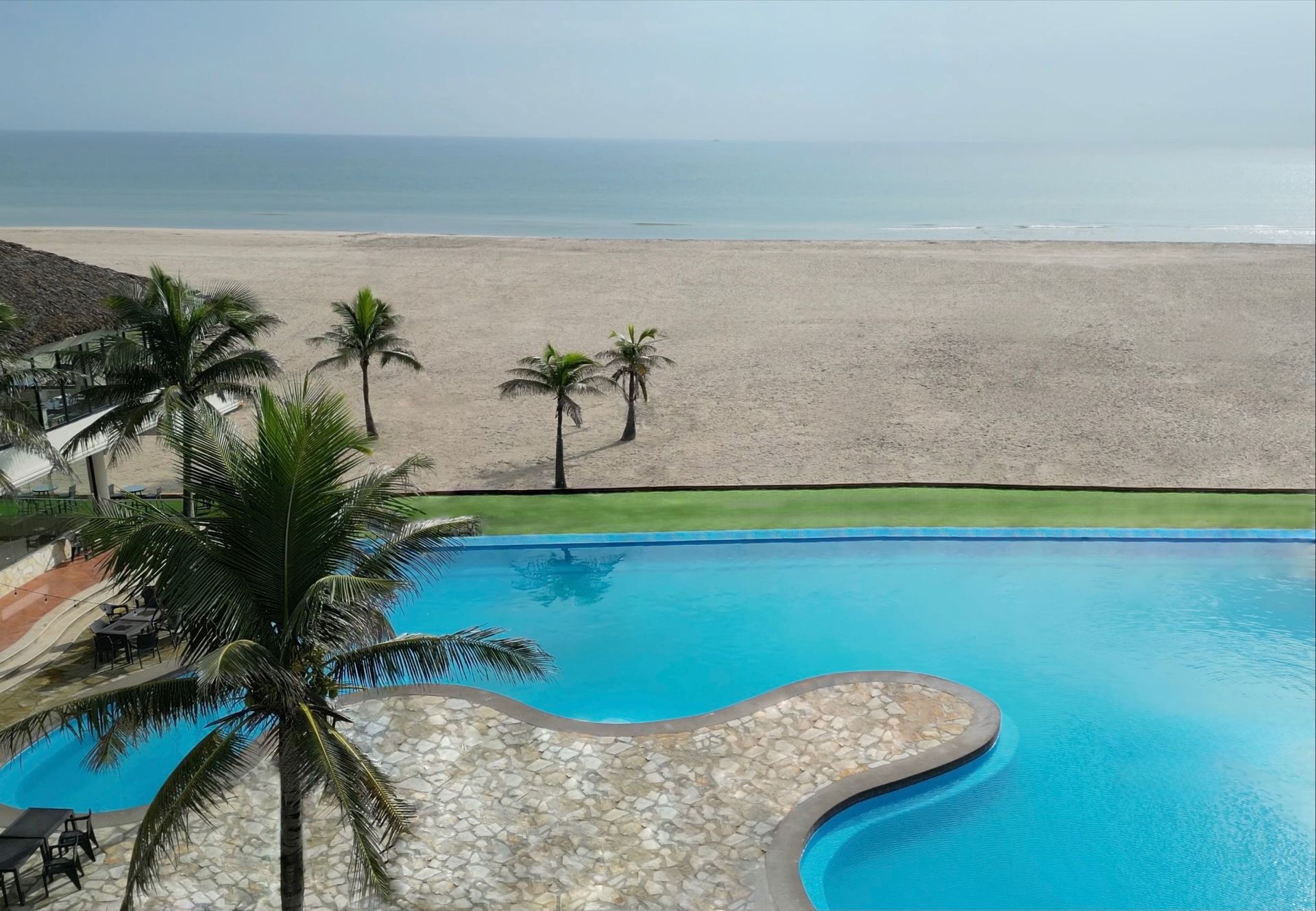 A large swimming pool surrounded by palm trees next to a beach.