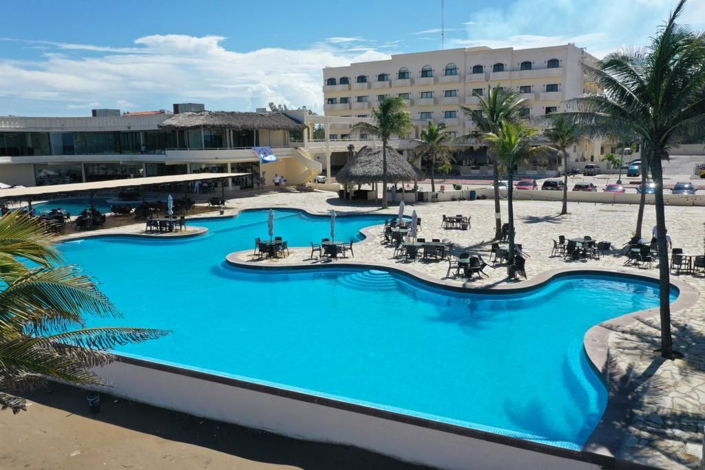 A large swimming pool surrounded by palm trees in front of a hotel.