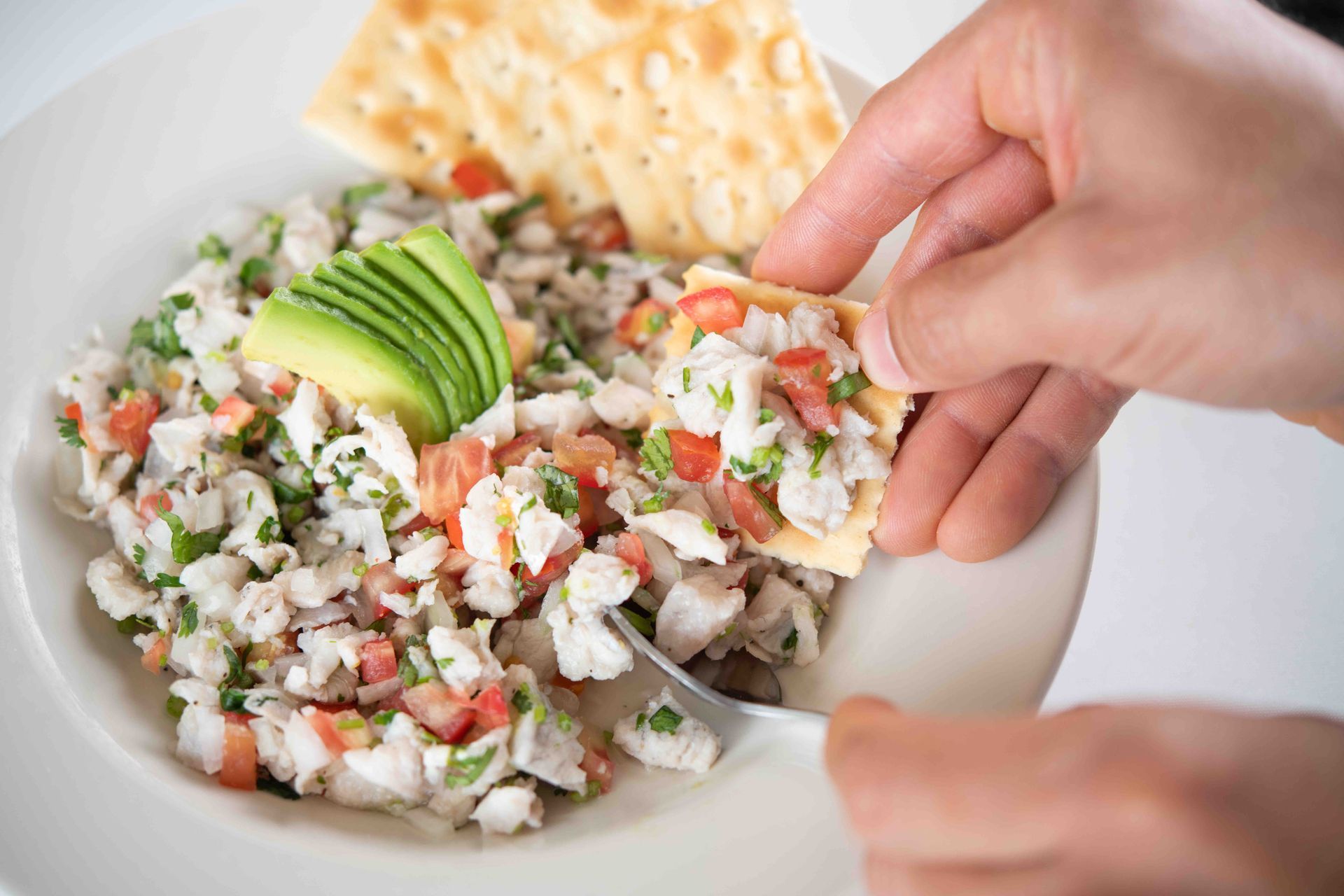 A person is dipping a cracker into a bowl of food.