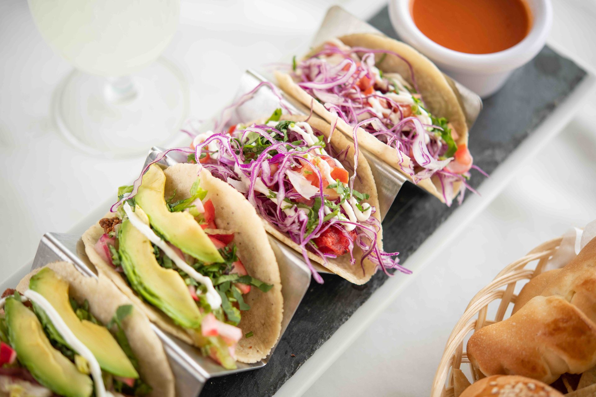 Three tacos with avocado , coleslaw and tomato sauce on a plate.