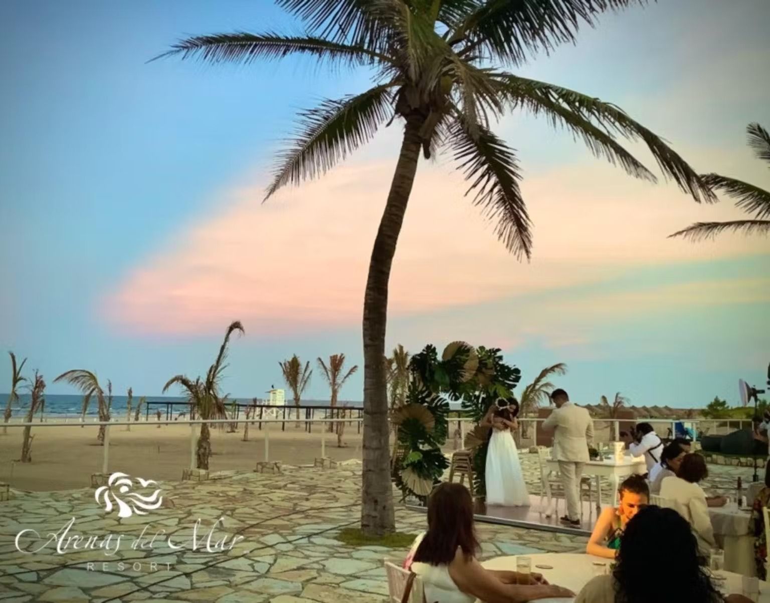 A group of people sitting at tables under a palm tree