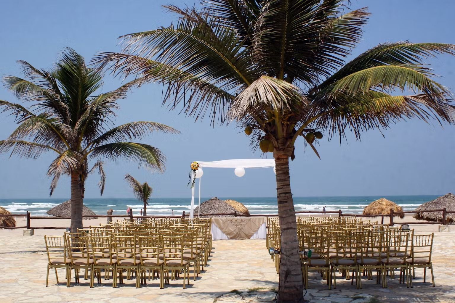 A beach with palm trees and chairs set up for a wedding