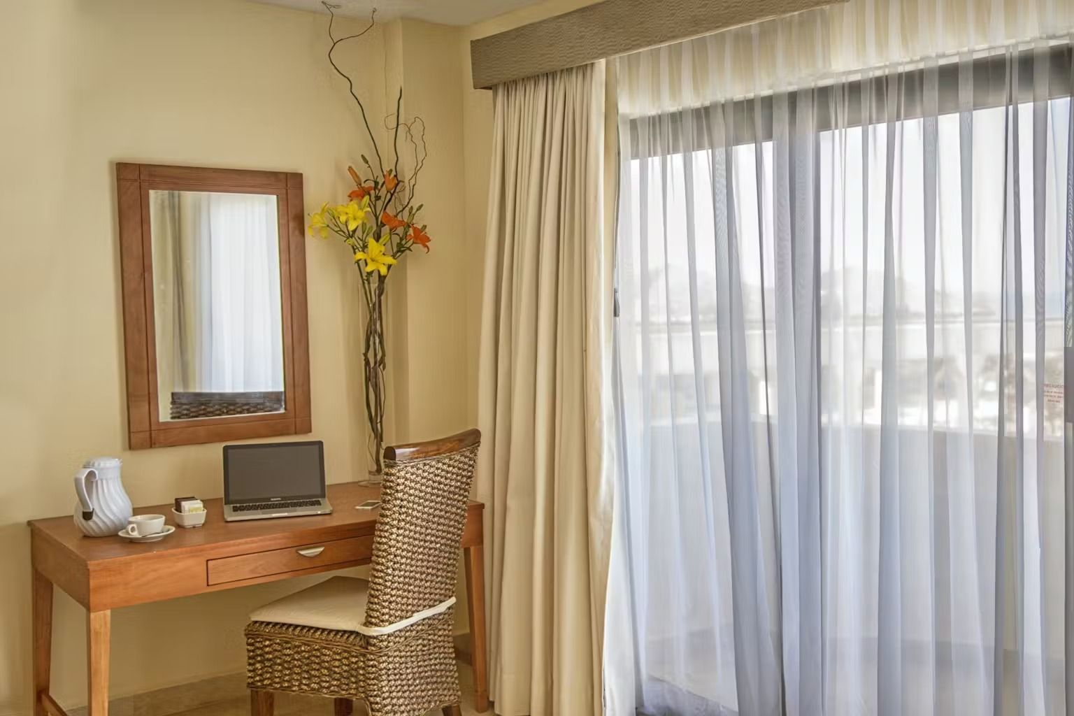 A room with a desk , chair , mirror and sliding glass doors.