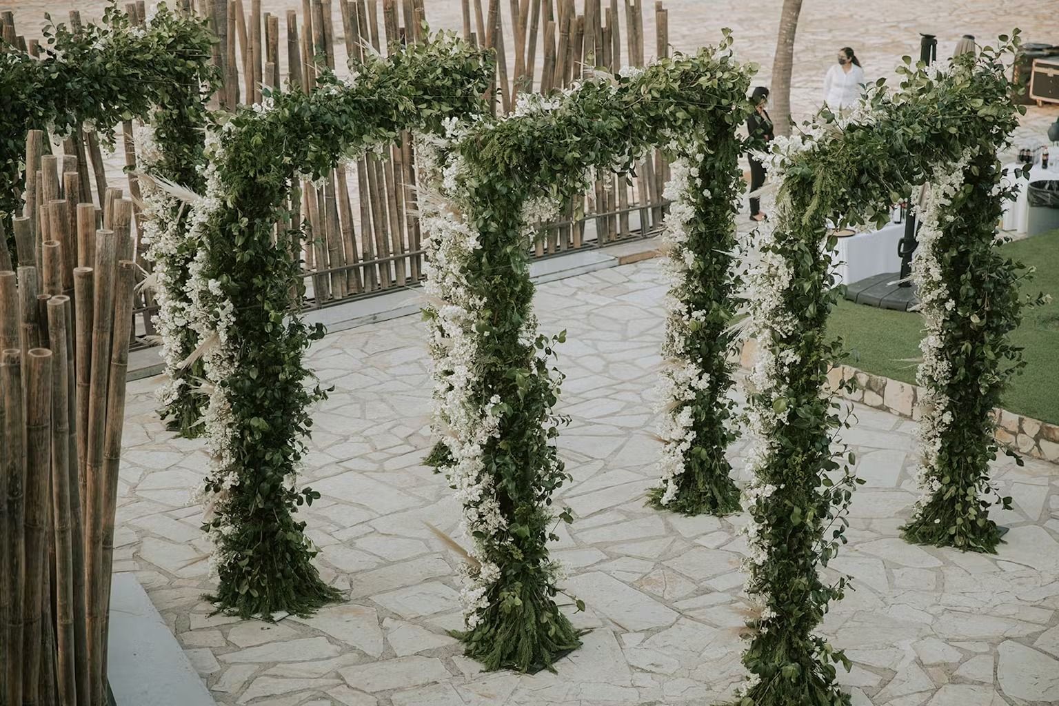 A wedding arch decorated with white flowers and greenery on a stone walkway.