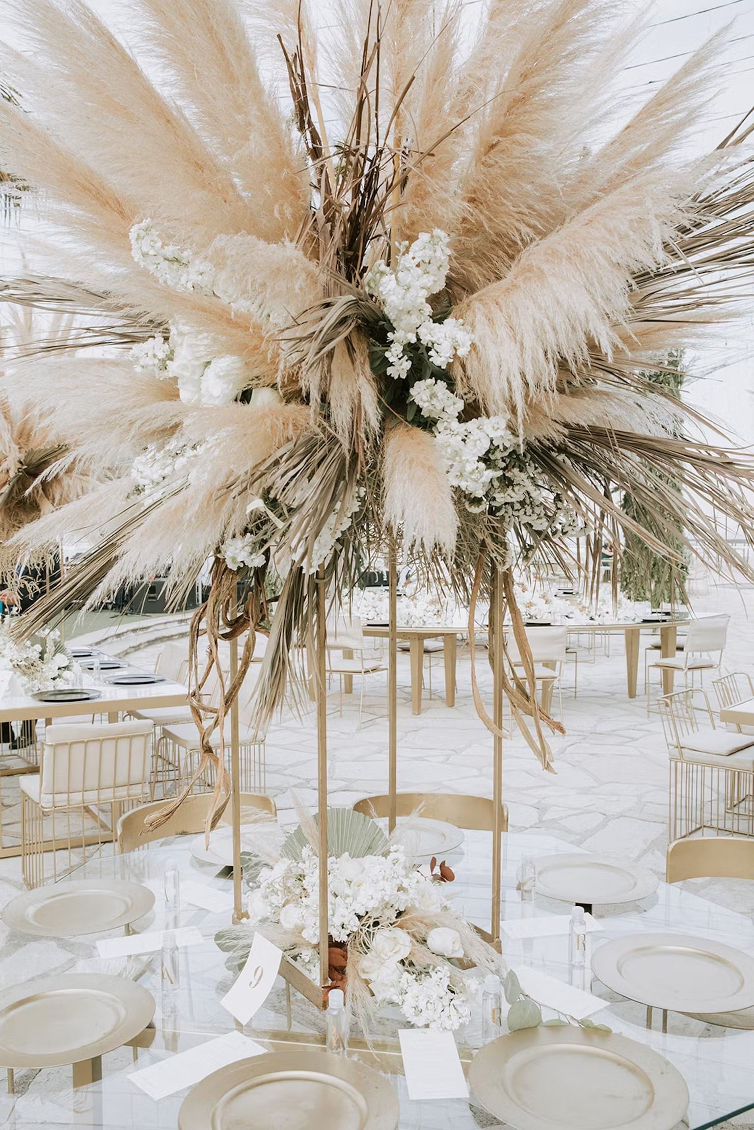 A table set for a wedding reception with a tall centerpiece of pampas grass and flowers.