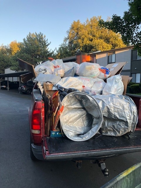 Pickup truck bed piled high with bagged trash and debris, parked on a roadside at sunset.