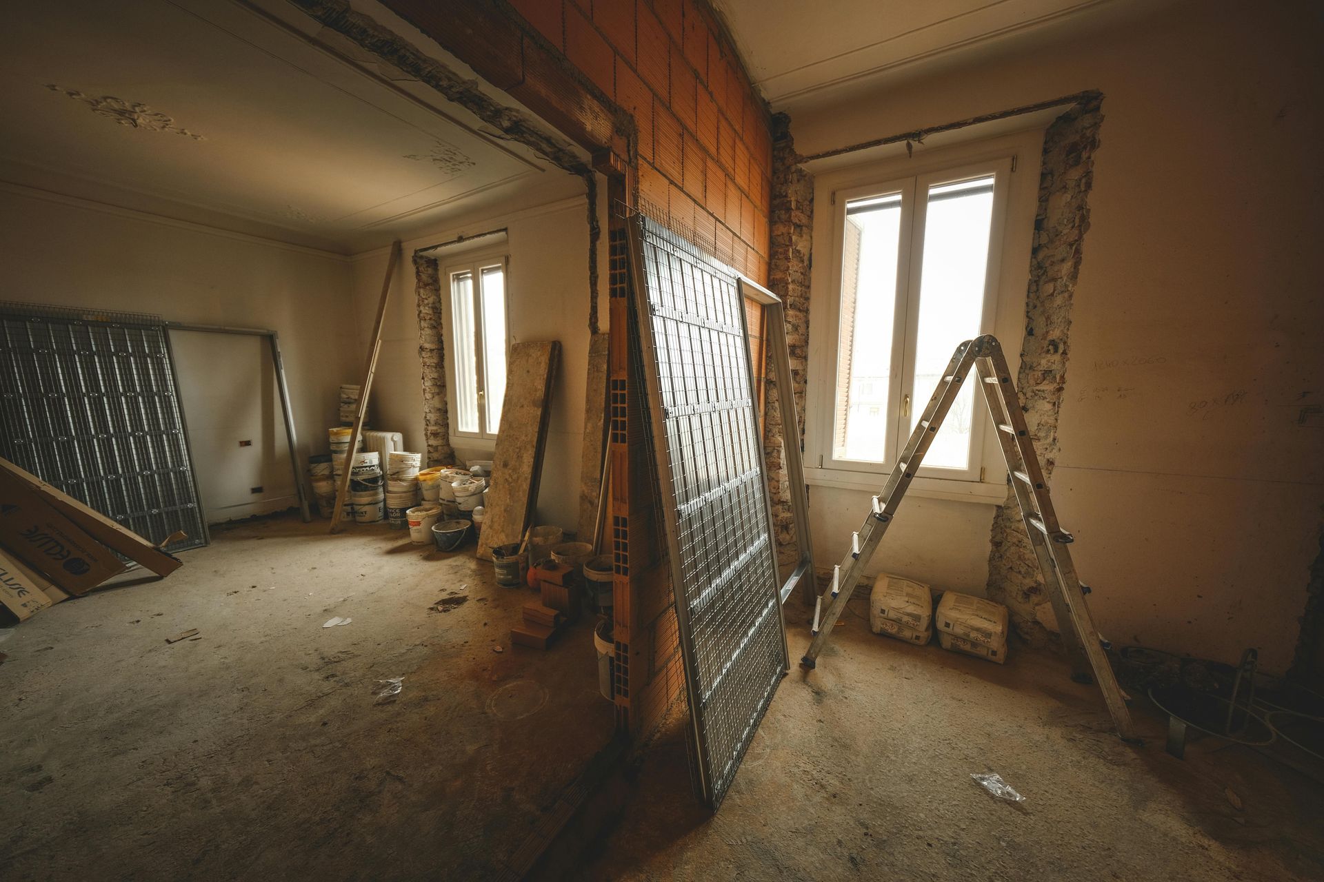 Renovation in progress in a bare room with ladders, tools, and a partially exposed brick wall.