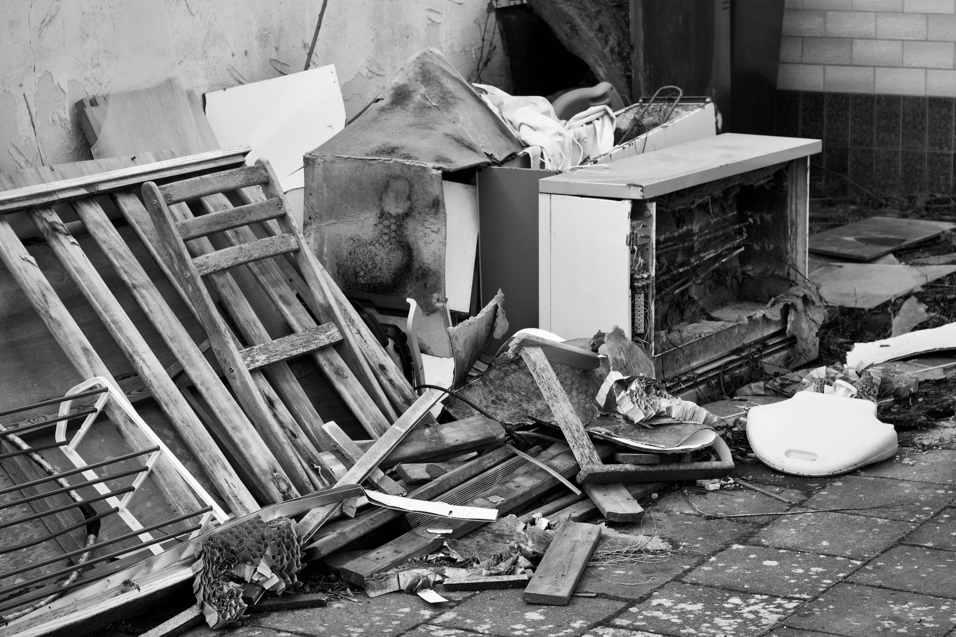 Scattered debris and broken furniture beside a wall, with a toppled pallet and damaged appliances outdoors.