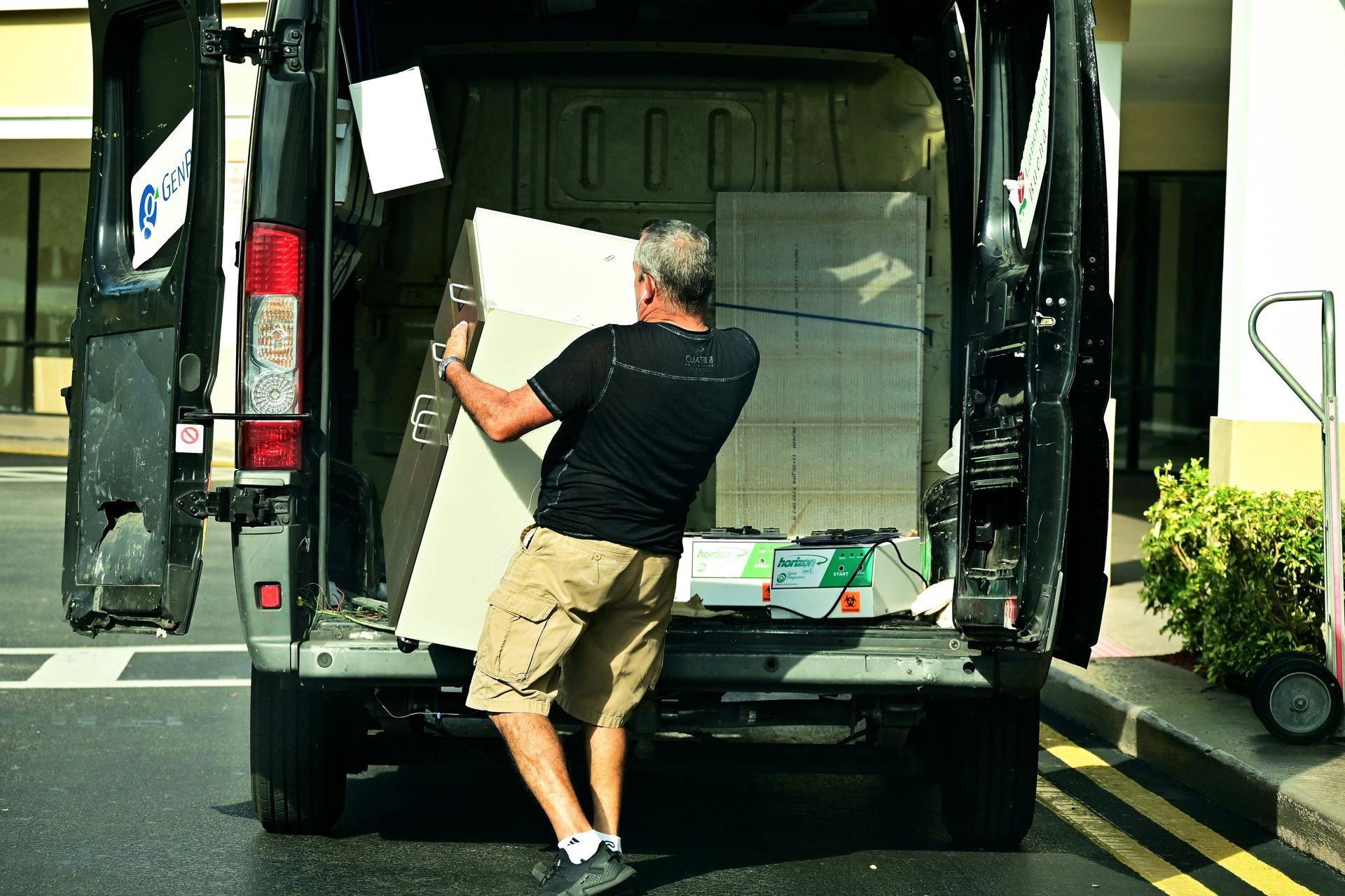 Man loading a large white panel into the back of a black van on a street
