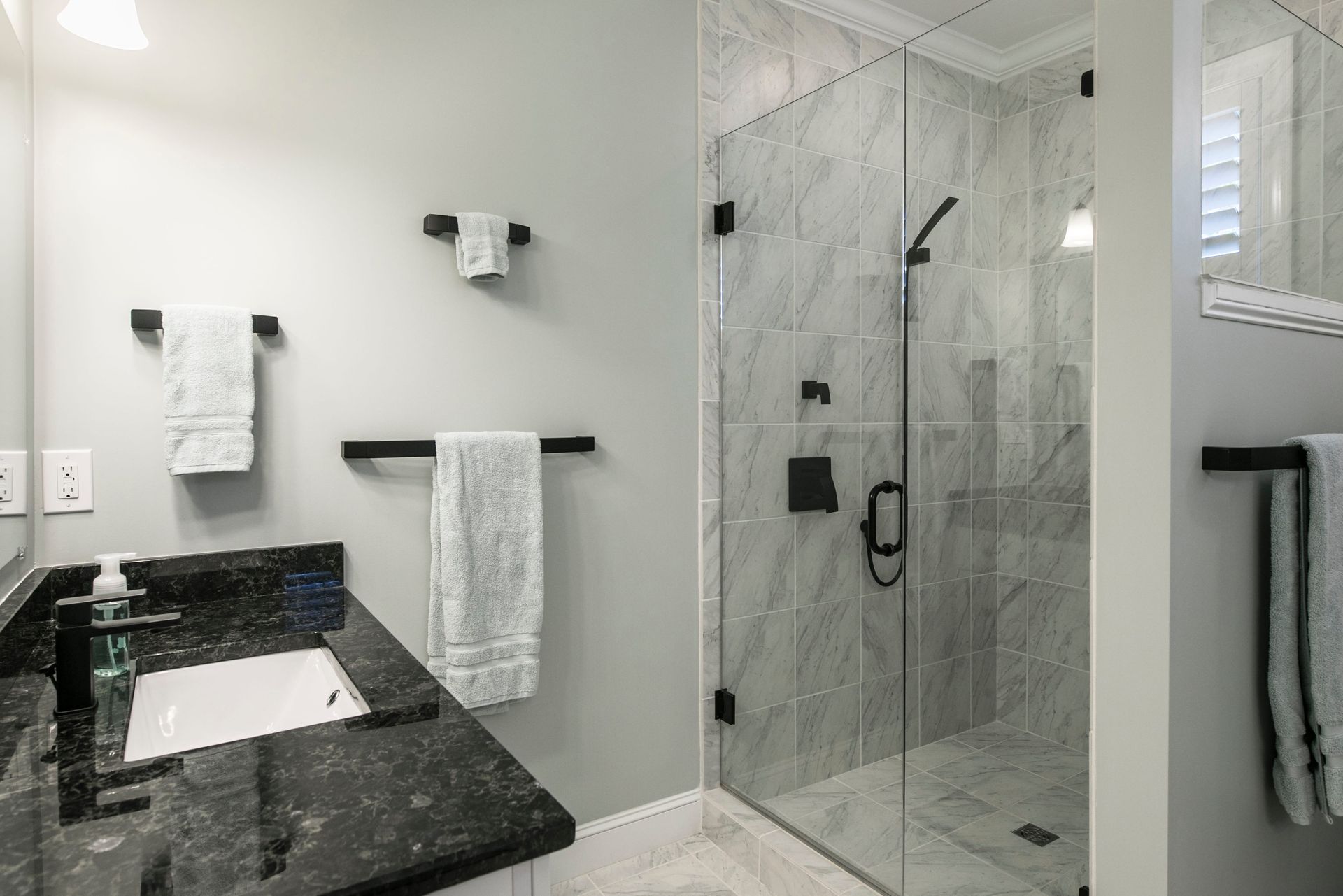 Bathroom with a glass shower, gray walls, black fixtures, granite countertop, and white towels.