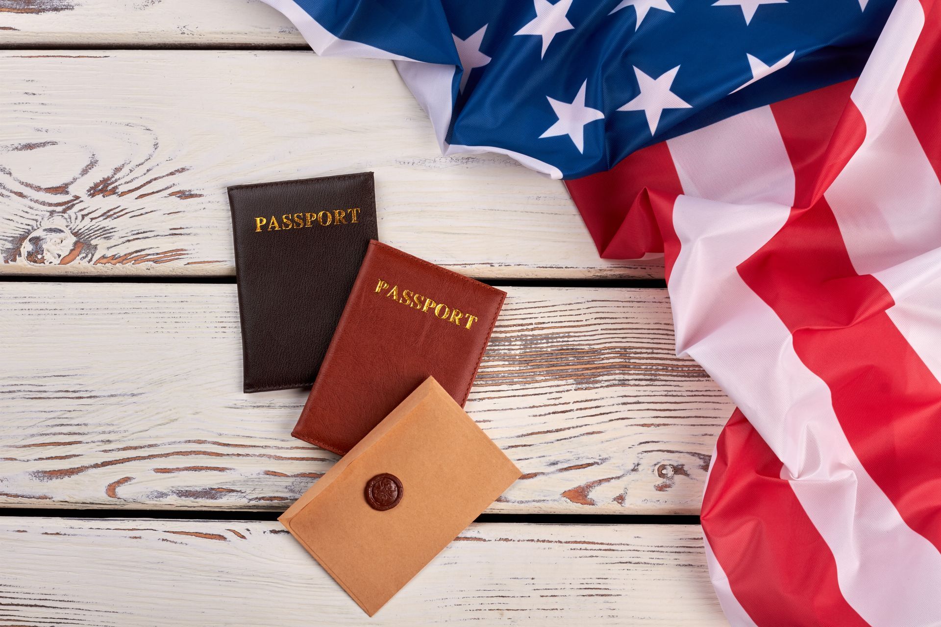 Three passports and an envelope with wax seal on a wooden surface next to American flag.