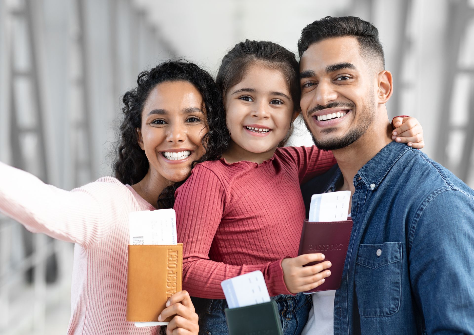Family of three smiling, holding passports and boarding passes, airport background.