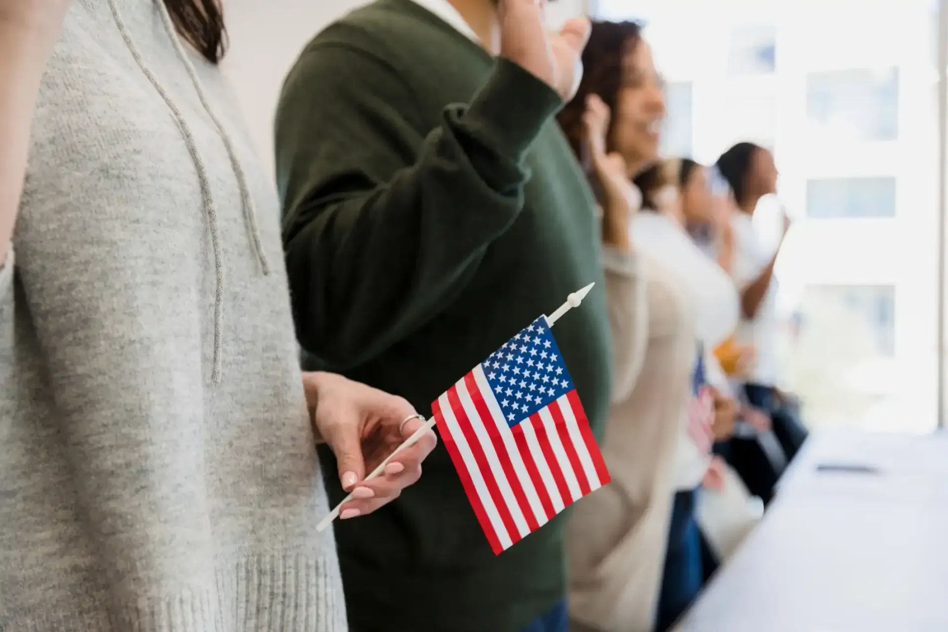People taking the U.S. citizenship oath, holding small American flags, indoors.