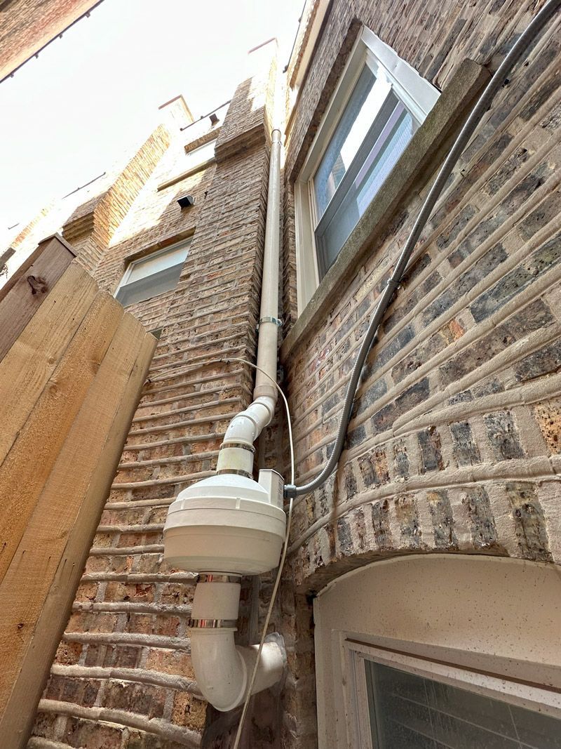 A white pipe is attached to the side of a brick building.