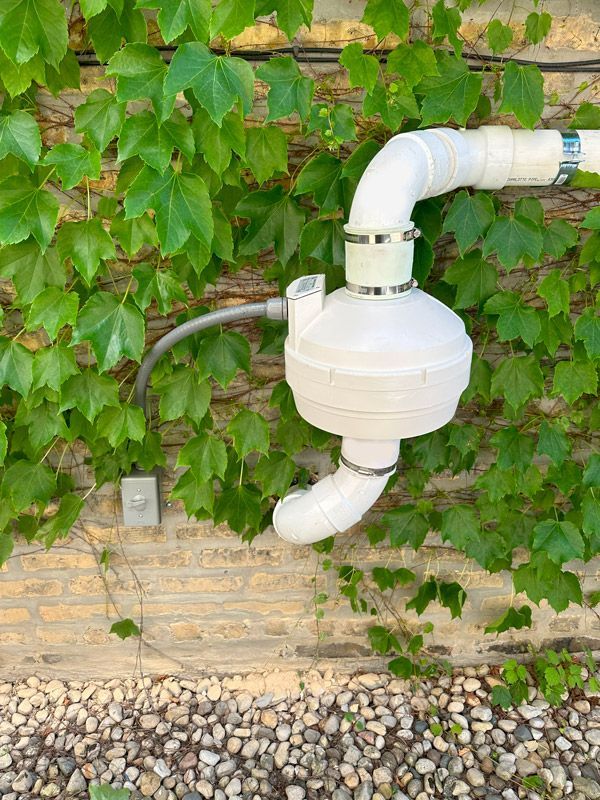 A white pipe is attached to a brick wall.