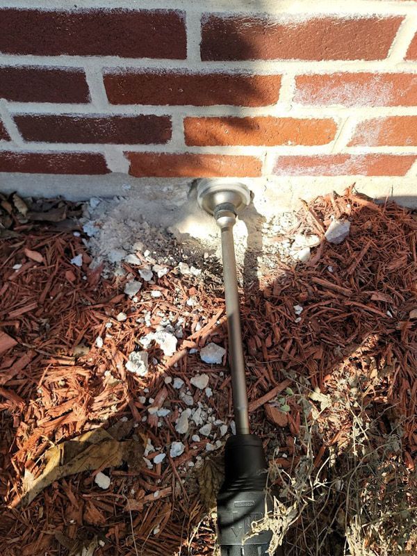 A hose is sitting in the dirt next to a brick wall.