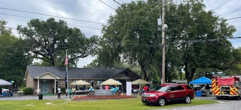 A community event with tents and a fire truck in front of a building with a large tree.