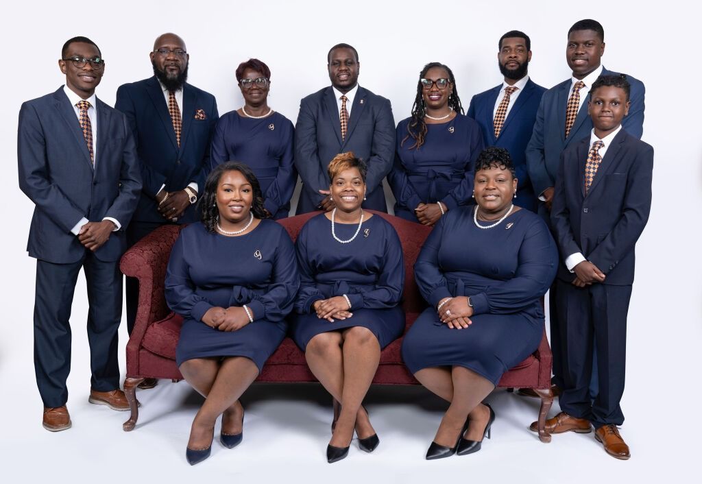 Group photo: people in navy suits and dresses, some seated on a burgundy couch, all facing the camera.