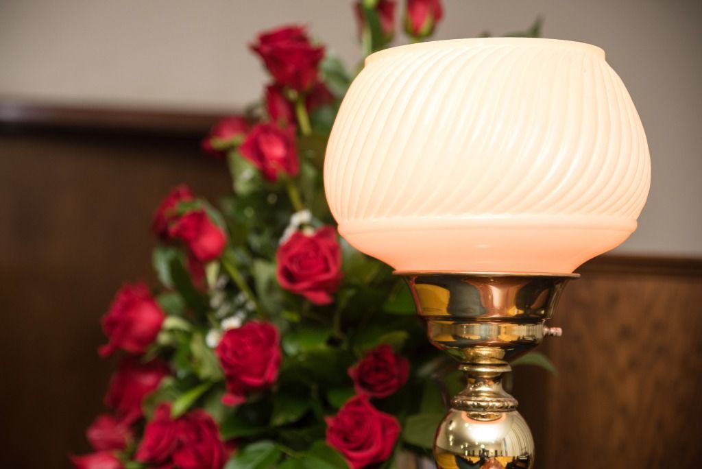 Brass lamp with a white globe next to a bouquet of red roses.