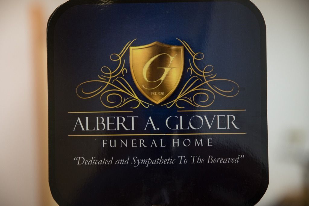 Dark blue sign for Albert A. Glover Funeral Home with gold logo and text.