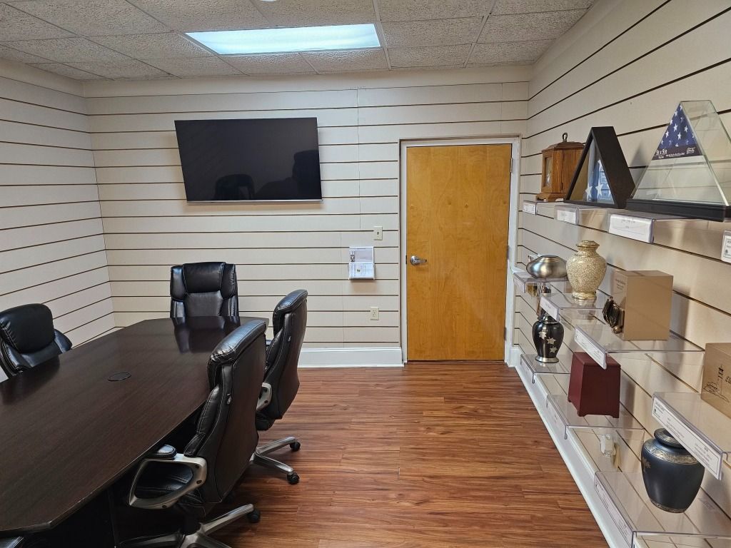 Conference room with long table, black chairs, TV, and display shelves with urns and memorabilia.