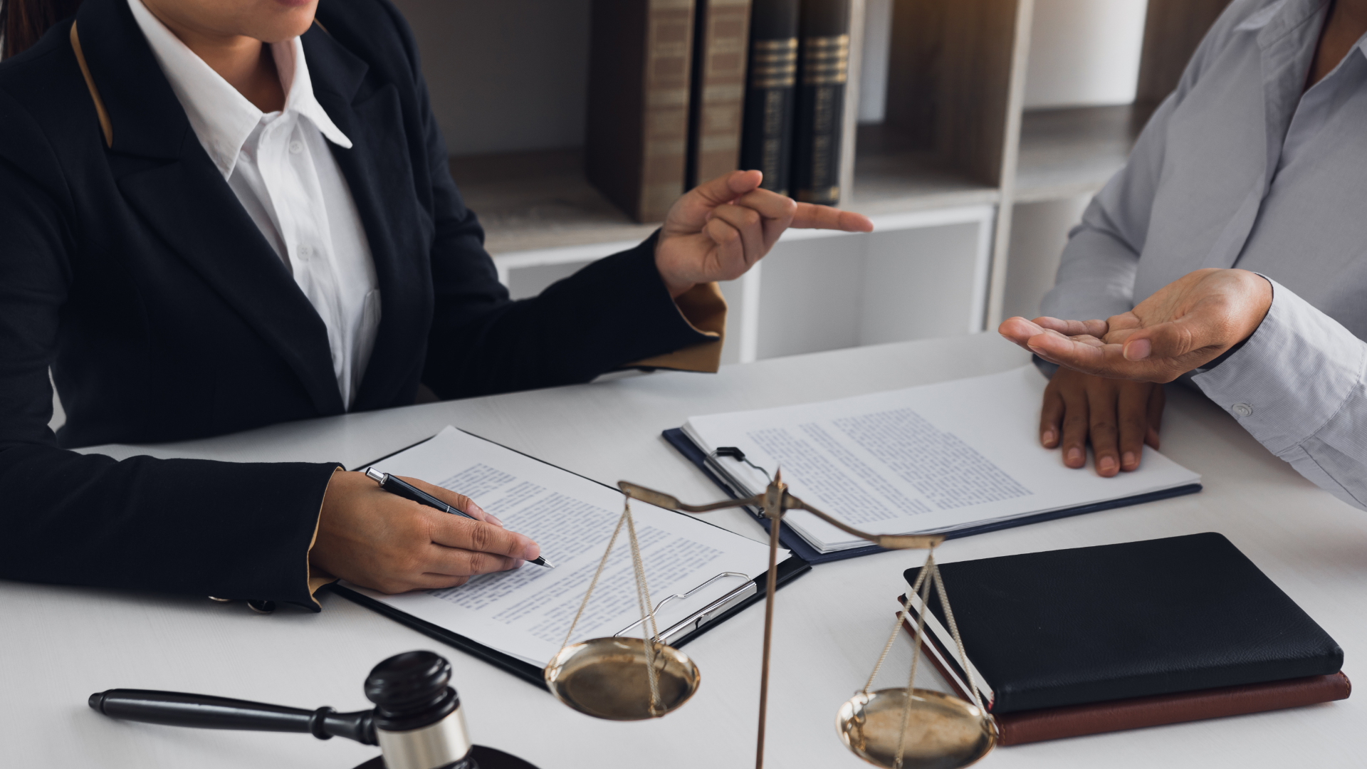 Two people at a desk, reviewing documents. Scales of justice, gavel, and books visible.