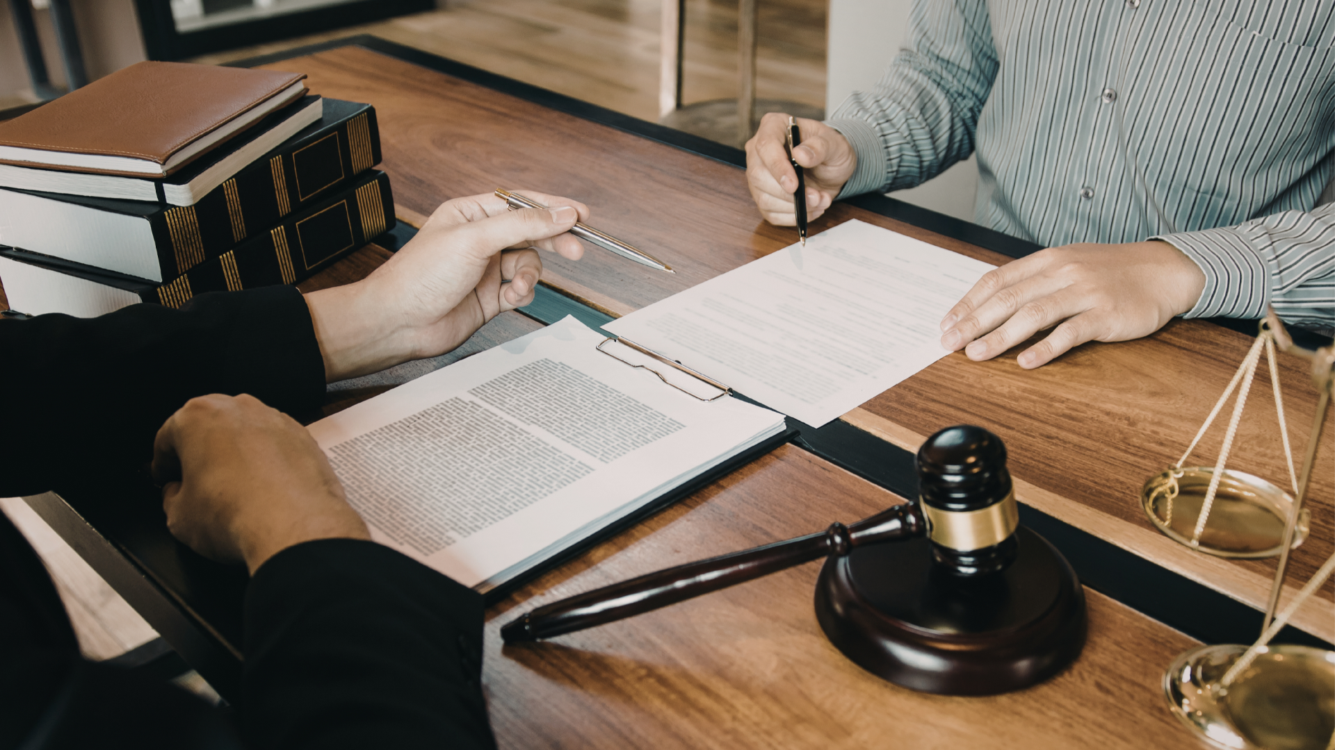 Two people at a desk review documents; a gavel and scales of justice are in the foreground.
