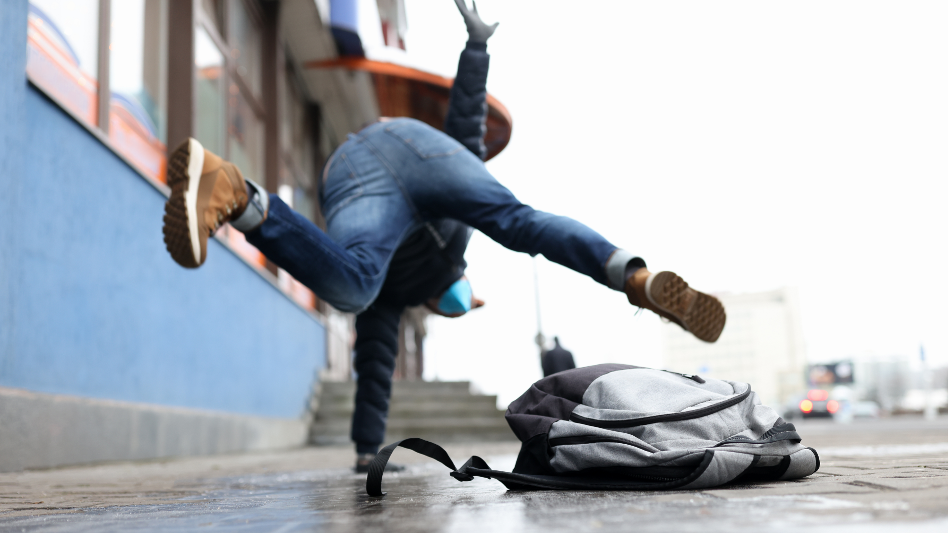 Person breakdancing on sidewalk, blue jeans and brown boots, backpack nearby.