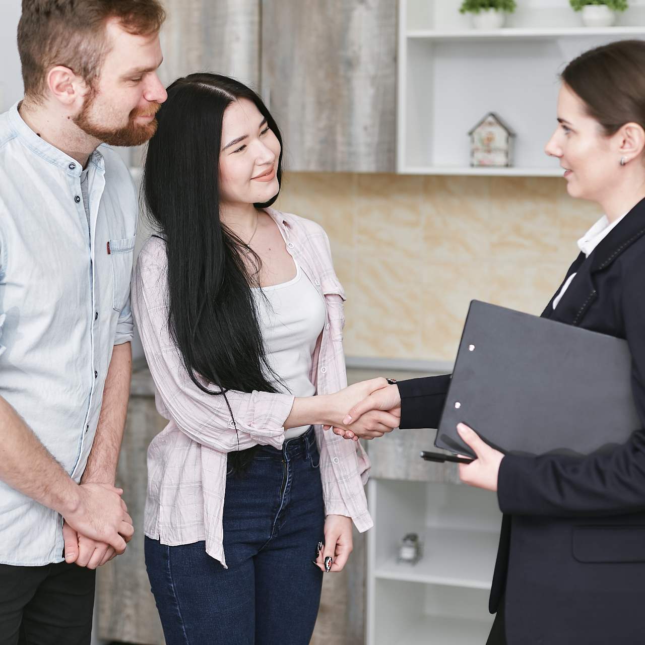 Couple shakes hands with a real estate agent inside a home.