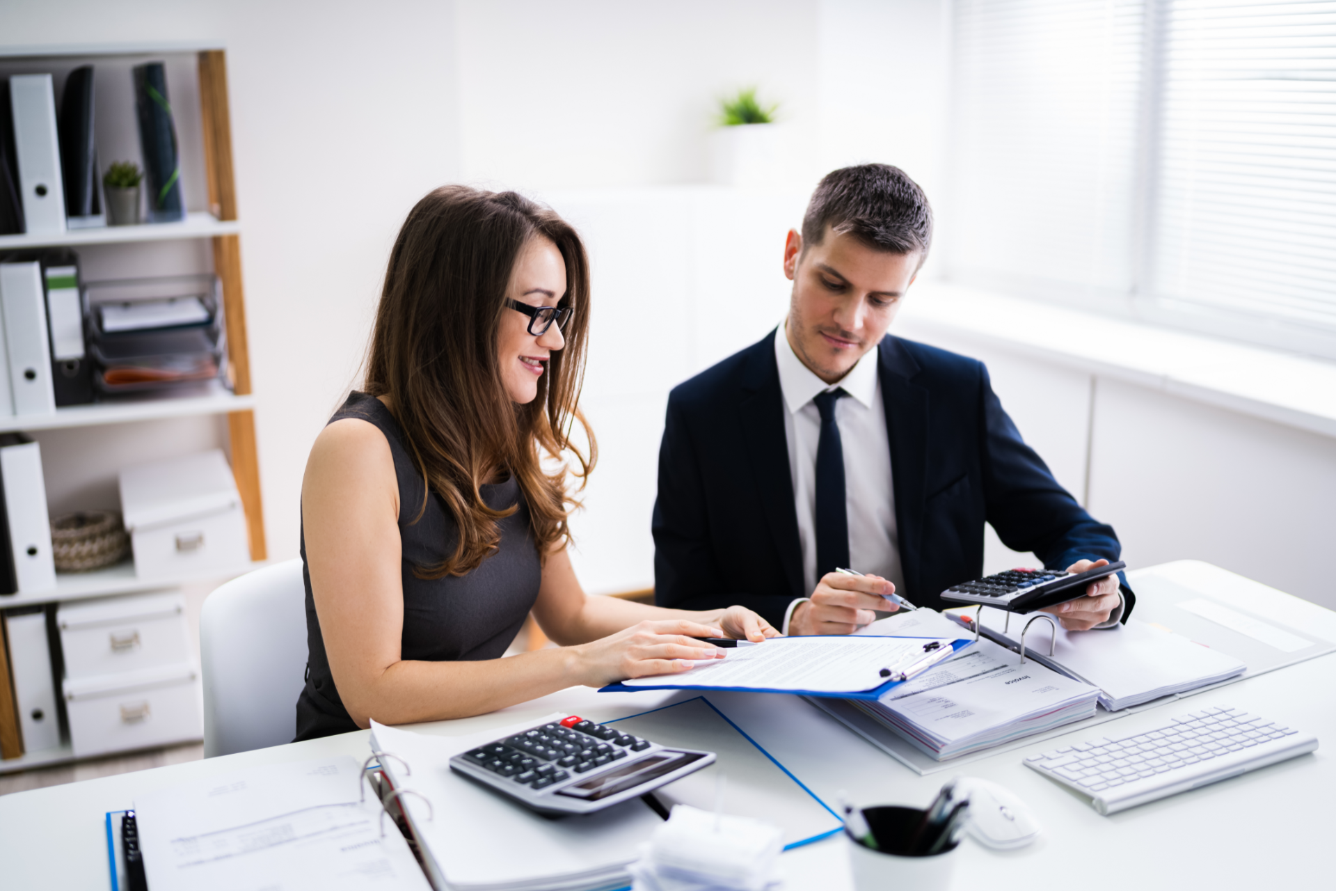 Two people reviewing documents and using calculators at a desk in an office.