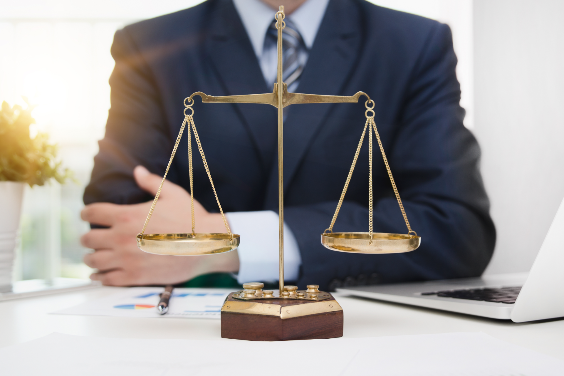 A justice scale in front of a person in a suit, with a laptop and papers.