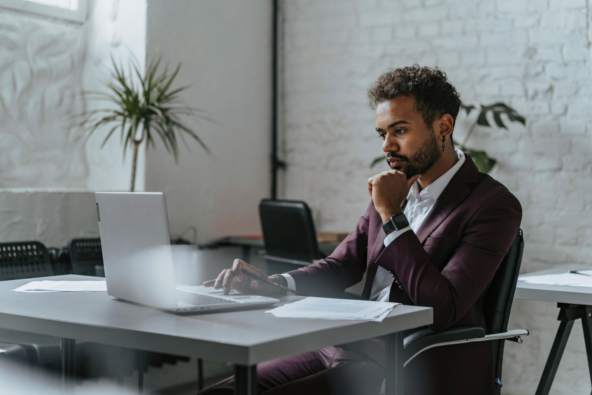 Man in maroon suit working on laptop at desk in office.