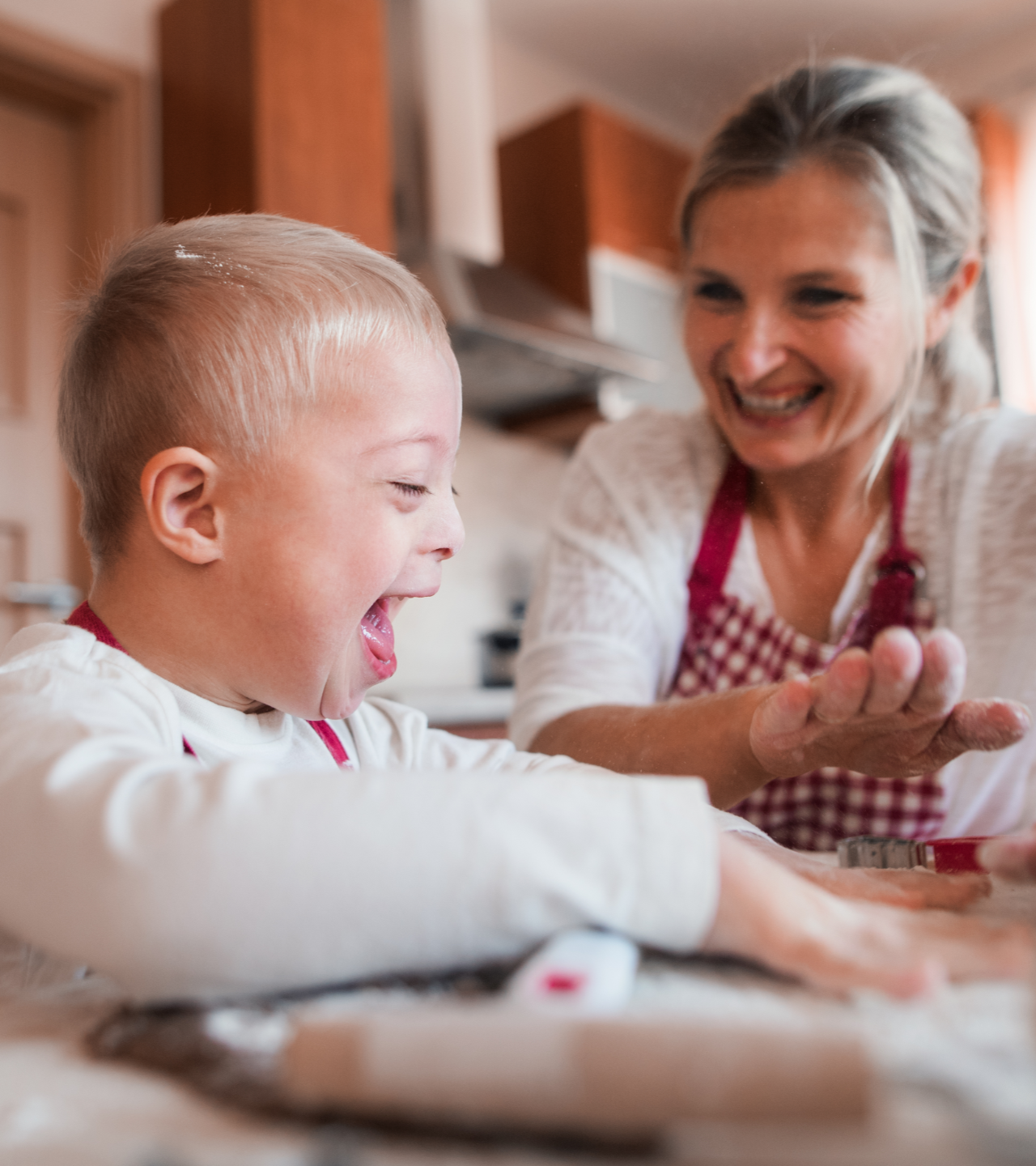 A smiling child and an adult bake together in a kitchen. The child is pressing dough.