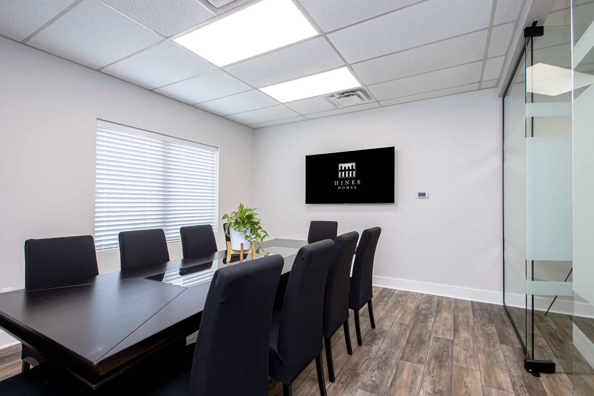 A modern conference room featuring a dark wood table with black chairs, a wall-mounted TV, and a small potted plant.