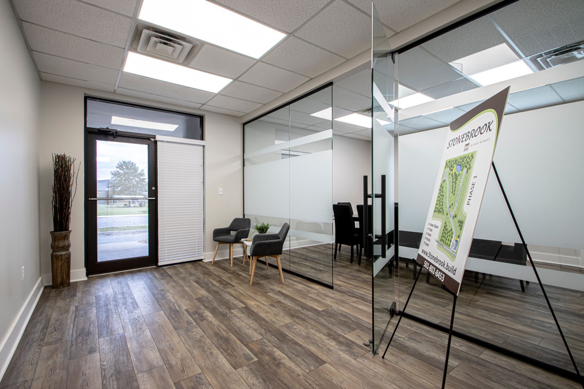 A modern office interior with a glass-walled conference room, wood floors, and a floor-standing map sign on an easel.