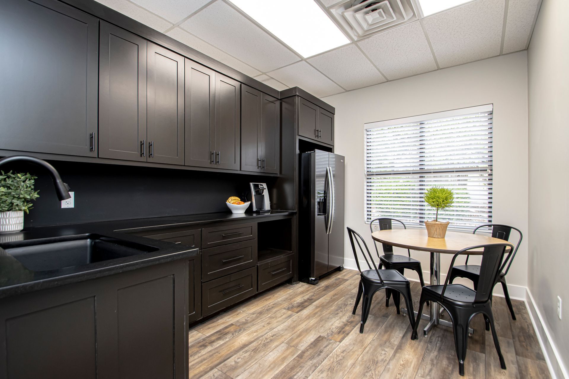 Modern kitchen breakroom with dark cabinetry, wood flooring, a stainless refrigerator, and a small round dining table.