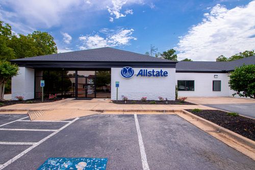An Allstate office building with a white brick exterior, blue signage, and an asphalt parking lot under a cloudy sky.