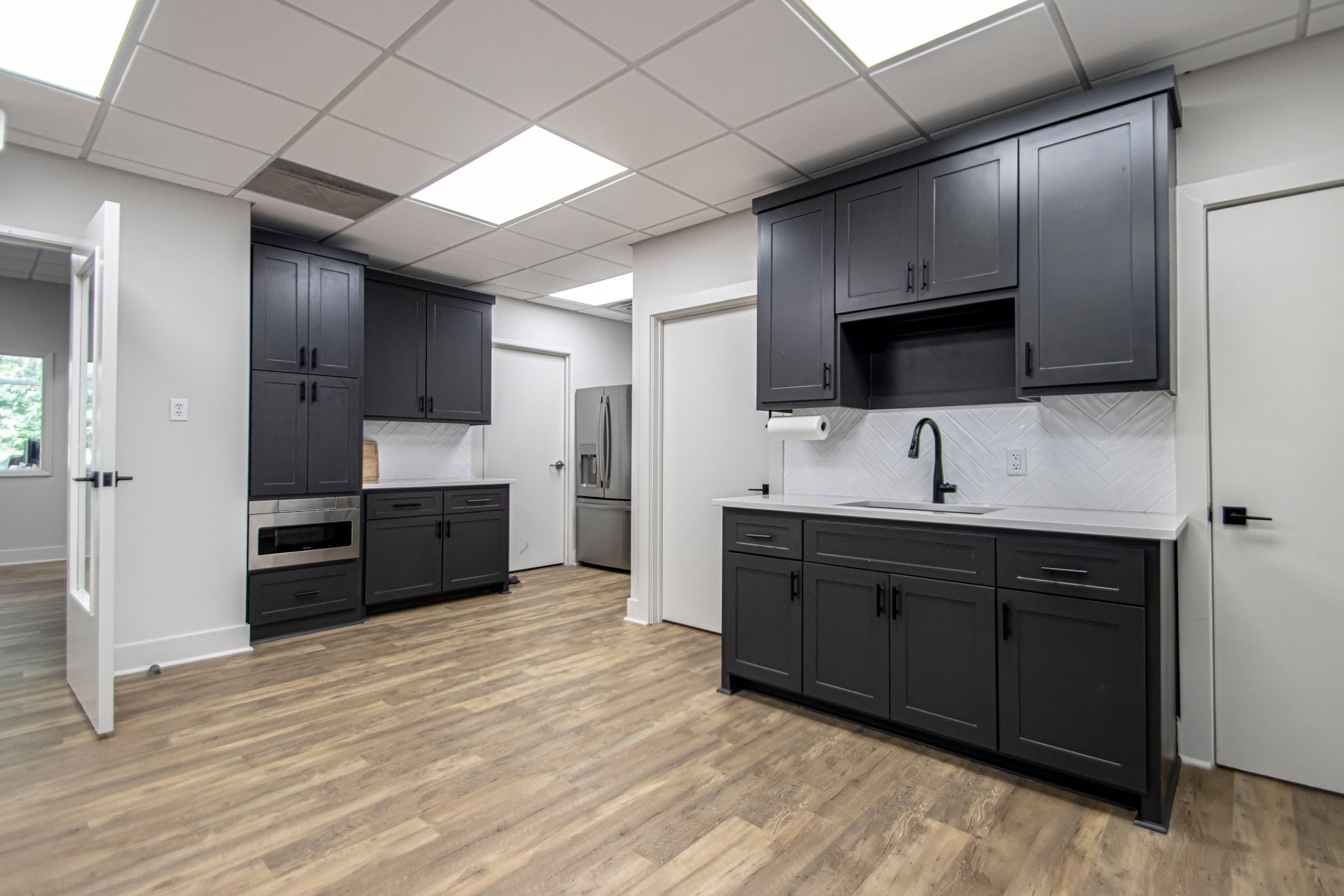 Modern breakroom with dark grey cabinets, light countertops, a sink, stainless steel appliances, and wood-look flooring.