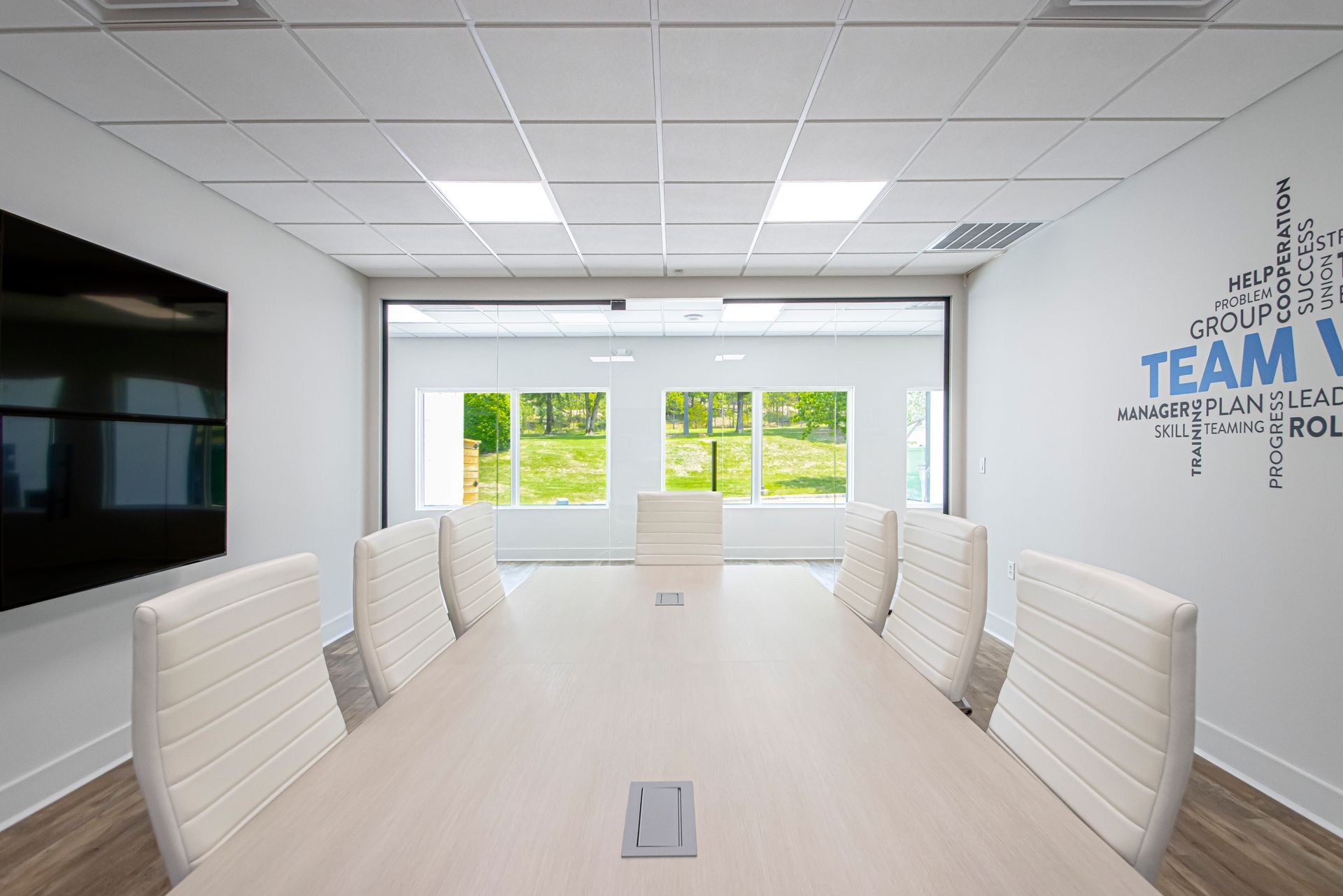 Empty conference room with a long table, white chairs, a wall-mounted screen, and a 